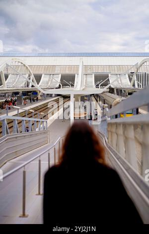 Femme avec de longs cheveux marchant dans les escaliers d'une gare moderne avec des détails architecturaux et des navetteurs en arrière-plan. Banque D'Images