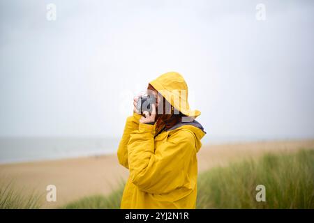 Photographe en imperméable jaune prend une photo un jour de plage nuageuse, Belgique Banque D'Images