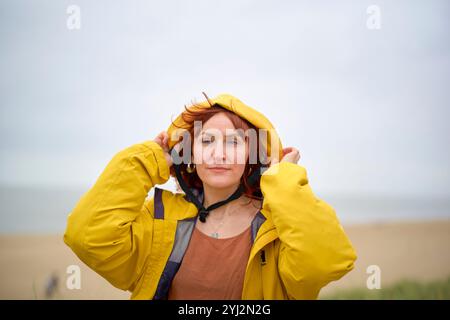 Femme dans un manteau à capuche jaune debout sur une plage avec un ciel nuageux en arrière-plan, Belgique Banque D'Images