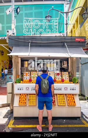 Un homme non asiatique vêtu de bleu, se tient devant un stand de jus et de limonade aux couleurs vives avec beaucoup d'agrumes exposés à Singapour Banque D'Images