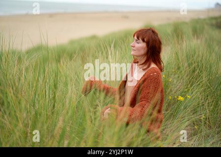 Femme dans un pull tricoté profitant d'un moment paisible dans les hautes herbes à la plage, Belgique Banque D'Images