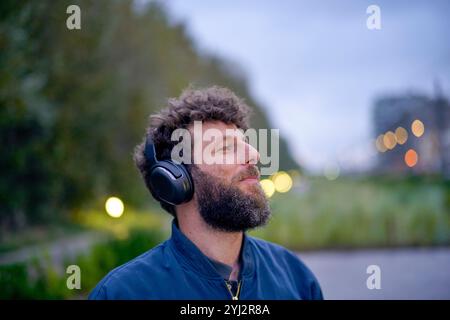 Homme avec des écouteurs appréciant la musique à l'extérieur au crépuscule, Belgique Banque D'Images