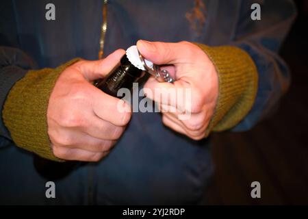 Gros plan d'une personne dans un pull vert ouvrant une bouteille de bière brune avec un couvercle blanc. Banque D'Images