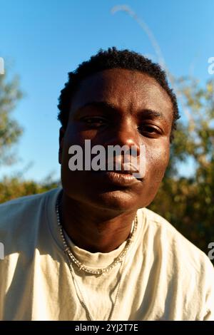 Portrait en gros plan d'un jeune homme avec une expression sérieuse debout à l'extérieur avec la lumière du soleil projetant des ombres sur son visage, Berlin, Allemagne Banque D'Images