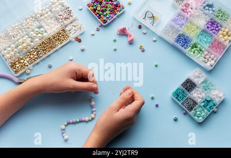 Une personne enfile habilement des perles sur une ficelle, entourée de divers récipients de perles colorées et d'outils sur une table d'artisanat lumineuse. Banque D'Images