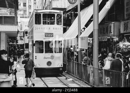 Un tramway approche de Hong Kong Market Station, entouré par les gens qui font du shopping et des affichages de marché animés de chaque côté. Banque D'Images