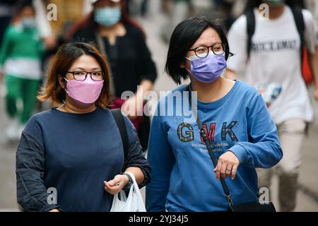 Deux femmes se promènent décontractées dans une rue animée de Hong Kong, portant des masques et engageant une conversation au milieu de la foule. Banque D'Images