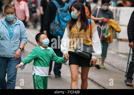 Une mère et son fils se promènent ensemble, vêtus de masques, au milieu d'une foule de piétons dans le centre de Hong Kong. Banque D'Images