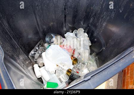 Regardant vers le bas dans un bac de recyclage gris partiellement rempli de bouteilles en plastique et de canettes en métal Banque D'Images