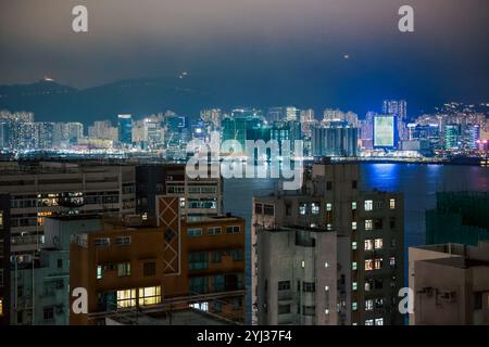 De grands bâtiments illuminent le port de lumières vibrantes lorsque la nuit tombe sur Hong Kong, mettant en valeur le paysage urbain dynamique de la ville. Banque D'Images