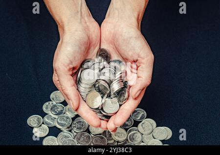 Pièces d'argent dans les paumes féminines sur fond noir. Notion d'importance du soutien financier social Banque D'Images