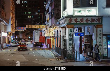 Un taxi longe une rue animée de Hong Kong, illuminée par des panneaux au néon et animée par de l'activité pendant la nuit. Banque D'Images