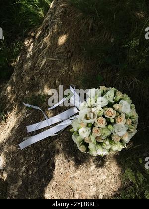 Un délicat bouquet de mariée avec des roses blanches et des rubans, orné d'anneaux de mariage, reposant sur un rocher naturel. Parfait pour romantique et sur le thème du mariage Banque D'Images