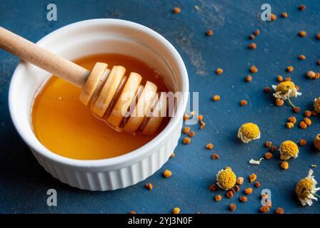 Miel biologique avec des fleurs de camomille et du pollen d'abeille, créant une composition naturelle et terreuse. Banque D'Images