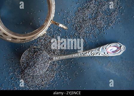 Gros plan de graines de pavot sur une cuillère en argent avec des graines dispersées, soulignant leur riche texture. Banque D'Images