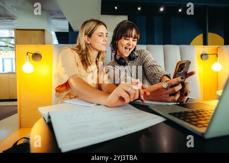 Deux étudiants de la génération Z capturent avec enthousiasme des selfies dans un environnement de bibliothèque dynamique, mettant en valeur le travail d'équipe et la collaboration. Banque D'Images