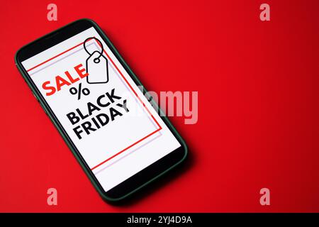 Gros plan d'un écran de smartphone affichant une vente en ligne Black Friday sur fond rouge vide Banque D'Images