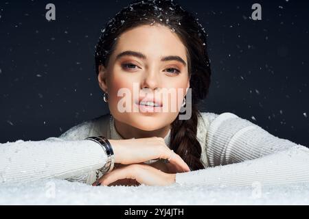 Une belle femme avec une expression chaleureuse repose son menton sur ses bras au milieu de flocons de neige qui tombent. Banque D'Images