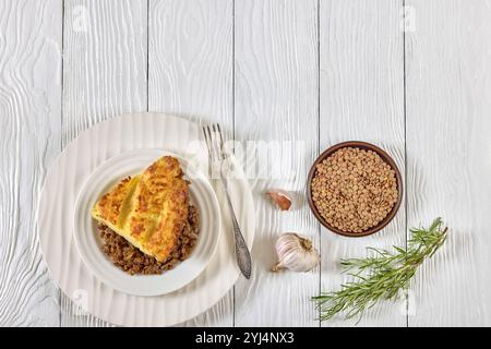 tarte végétalienne aux bergers de lentilles cuites garnie de purée de pommes de terre sur assiette blanche avec fourchette sur table en bois avec romarin, vue horizontale d'en haut, Banque D'Images