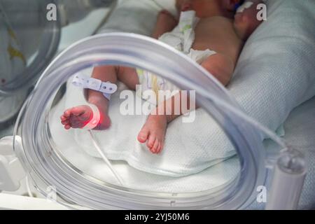 Vue rapprochée d'un bébé prématuré dans l'incubateur et tenu par une mère aimante Banque D'Images