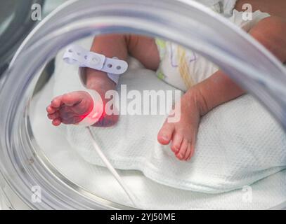 Vue rapprochée d'un bébé prématuré dans l'incubateur et tenu par une mère aimante Banque D'Images