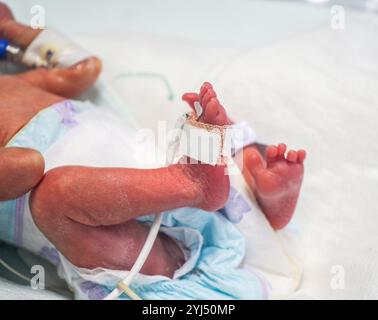 Vue rapprochée d'un bébé prématuré dans l'incubateur et tenu par une mère aimante Banque D'Images