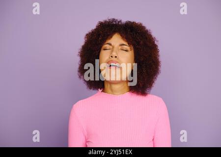 Une jeune femme afro-américaine met en valeur ses émotions brutes, vêtue de rose, avec un décor violet captivant. Banque D'Images