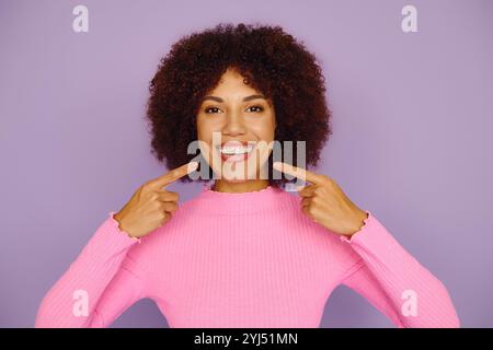 Une jeune femme afro-américaine met en valeur le pur bonheur et les bretelles, souriant brillamment tout en portant des vêtements roses décontractés. Banque D'Images