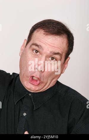 Homme d'âge moyen, avec les cheveux foncés sur fond blanc, fait un visage inhabituel, plongeant, hurlant, éternuant, étouffant, très expressif, expression Banque D'Images