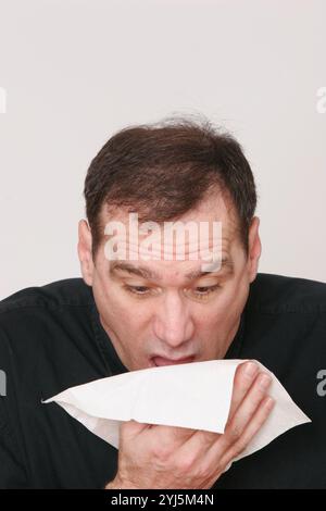 Homme d'âge moyen, avec les cheveux foncés sur fond blanc, fait un visage inhabituel, plongeant, hurlant, éternuant, étouffant, très expressif, expression Banque D'Images