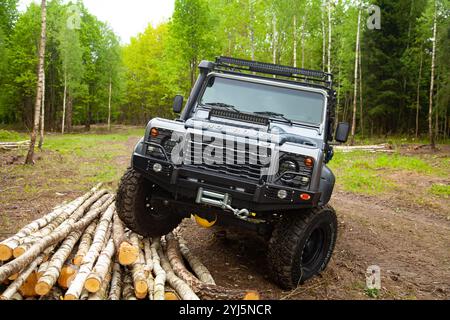 Land Rover Defender équipé dans la forêt avec tout l'équipement nécessaire - treuil, lumière supplémentaire, pneus de boue et tuba, se tient sur les bûches Banque D'Images