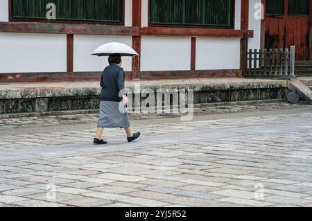 Femme âgée avec un parapluie marchant sur l'allée pavée à côté d'une maison traditionnelle japonaise, à Nara. Banque D'Images