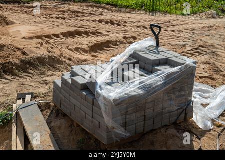 Une pile de briques grises est enveloppée dans du plastique sur un chantier de construction. Banque D'Images