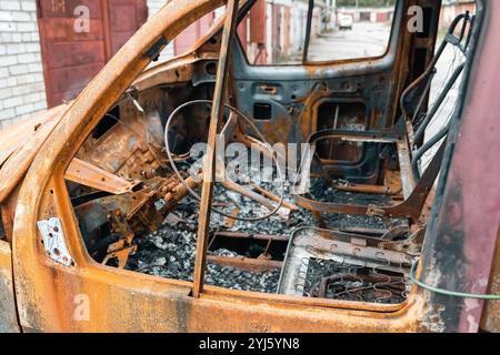 Gros plan d'une voiture brûlée rouillée dans une cour abandonnée montrant le volant et les sièges Banque D'Images