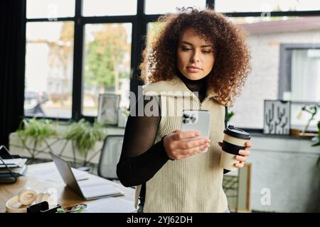 Immergée dans son smartphone, une femme savoure une tasse de café fumant dans un espace de travail confortable. Banque D'Images