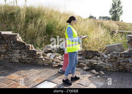 Une experte en assurance femme avec sa tablette examinant les dommages à un mur de pierre sur le lieu de l'accident Banque D'Images