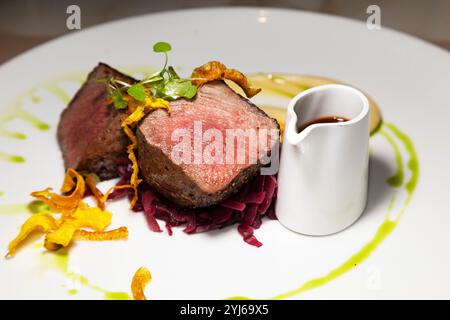 Longe de venaison servie avec panais croustillant, chou rouge braisé et pichet de jus. Banque D'Images