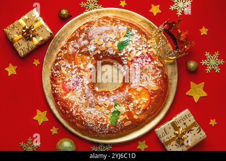 Vue de dessus du Roscon de reyes sur une plaque dorée avec étoiles dorées, coffrets cadeaux et couronne des sages sur fond rouge. Kings Day concept espagnol th Banque D'Images