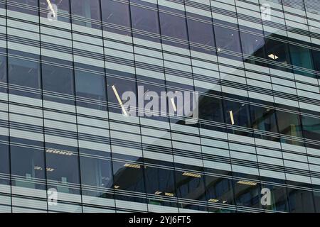 Une vue rapprochée de l'extérieur d'un bâtiment moderne en verre et en métal, présentant une grille de fenêtres et des lignes horizontales. Les fenêtres reflètent l'environnement Banque D'Images