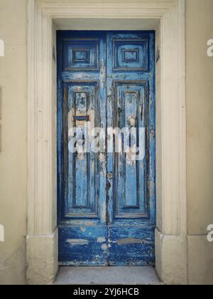 Porte en bois bleu vieilli avec peinture écaillée, située dans un cadre en pierre historique à la Valette, Malte. Banque D'Images