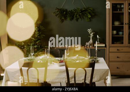 Table en bois décorée avec guirlande de pin au centre de la table et entourée d'argenterie polie et de verres en cristal, salle entièrement équipée avec des meubles en bois et des décorations pour Noël Banque D'Images