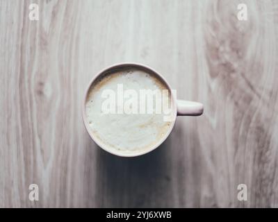 Une tasse de café est assise sur une table en bois. Le café est chaud et fumant, et la tasse est rose. Concept de chaleur et de confort, car le café est une boisson populaire pour la détente et la socialisation Banque D'Images