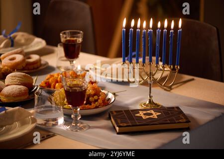 Gros plan moyen de bougies allumées bleues en chandelier doré, Torah avec étoile de David sur la couverture et différents plats sur le dessus de table Banque D'Images