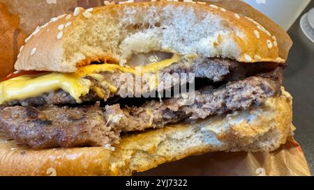 Un double cheeseburger partiellement mangé sur un pain aux graines de sésame, avec deux galettes de bœuf, du fromage fondu et une pointe de ketchup. Banque D'Images