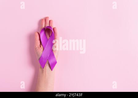 Ruban violet dans la main des femmes sur fond rose Banque D'Images