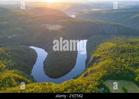 Alors que le soleil se couche, la rivière Vltava reflète des teintes vibrantes et encercle des collines verdoyantes en Tchéquie, créant une vue imprenable qui capture la beauté de la nature au crépuscule. Banque D'Images