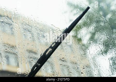 Des gouttes de pluie tombent en cascade sur le pare-brise d'une voiture, déformant le paysage urbain au-delà. Les essuie-glaces de pare-brise se déplacent de façon rythmique, luttant contre les pluies pendant une trans Banque D'Images