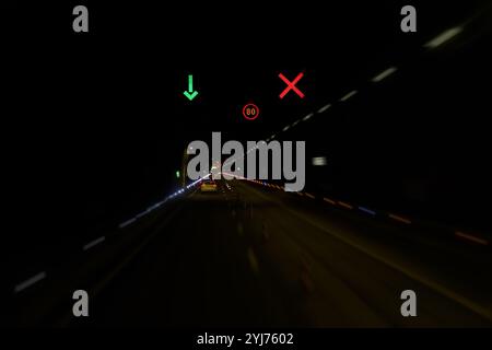 Un tunnel la nuit est rempli de traînées de lumière provenant de véhicules en mouvement. Les feux de circulation guident les conducteurs, mettant en valeur un affichage vibrant de rouge et vert L. Banque D'Images