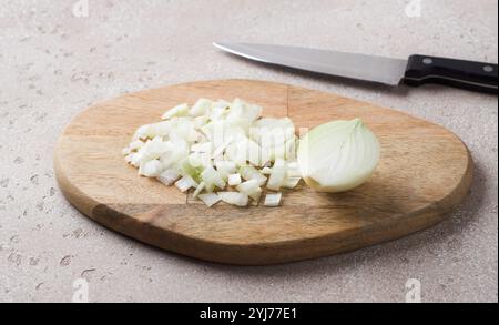Planche de bois avec oignon haché et couteau sur une table en pierre beige, vue de dessus Banque D'Images