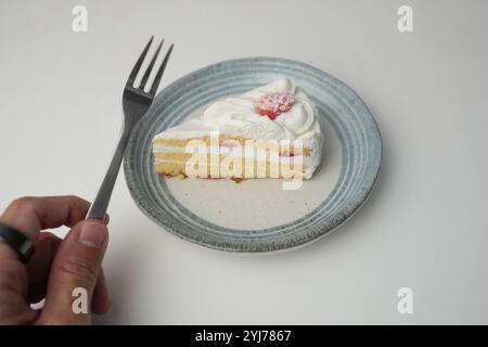 Un petit sablé japonais à la fraise sur une élégante assiette japonaise sur une table blanche et la main d'un homme tenant une petite fourchette pour le manger. Banque D'Images